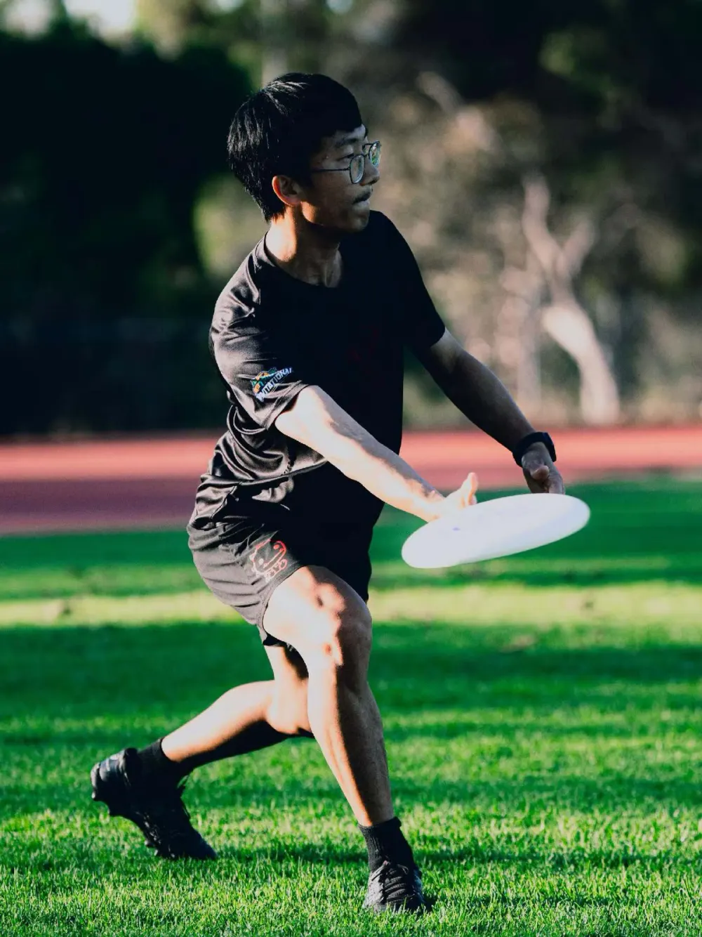Yuelin mid-throw on a grass field at golden hour, releasing a white disc