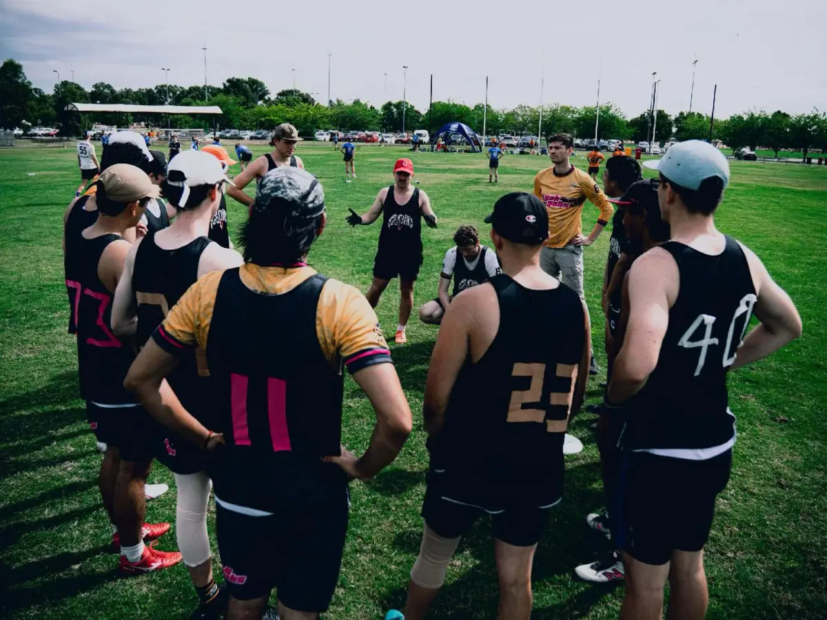 An ultimate team in a huddle on a tournament field, seen from behind